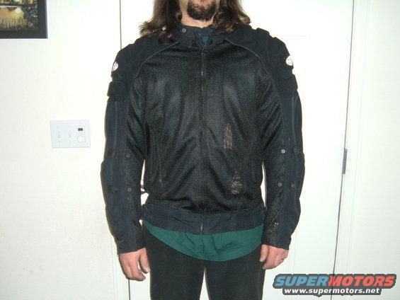 Person wearing a black mesh motorcycle jacket over a green shirt and dark pants