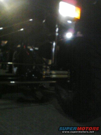 Truck front end with headlight on. Shows suspension components and tire