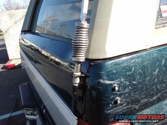 CB antenna spring mount attached to the rear of a dark green SUV. Scratches visible on the body panel