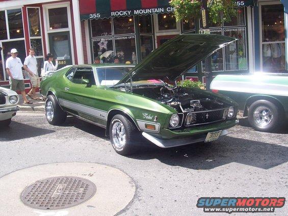 Green 1971 Ford Mustang with hood open, showing engine. Chrome wheels, silver side stripe. Parked on street