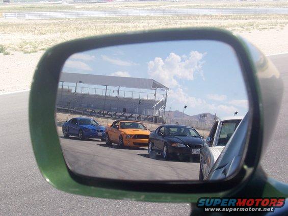three Mustangs on track, viewed in side mirror