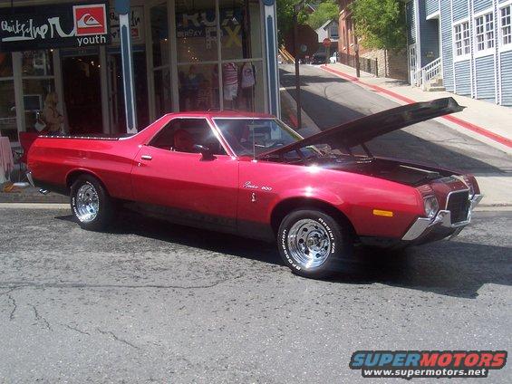 Red 1972 Ford Ranchero parked on street, hood open, chrome wheels, Quiksilver store in background