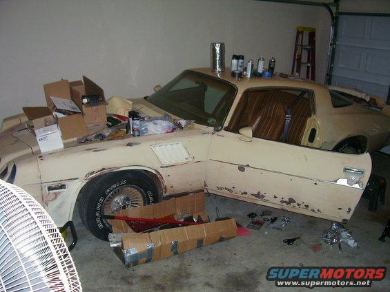 1979 Chevrolet Camaro in a garage, door open, with boxes and spray cans on the hood and roof
