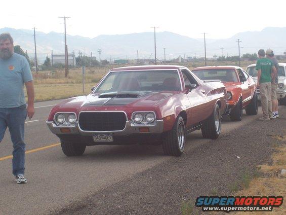 Red 1972 Ford Gran Torino Sport with black hood scoop and grille, parked on a road