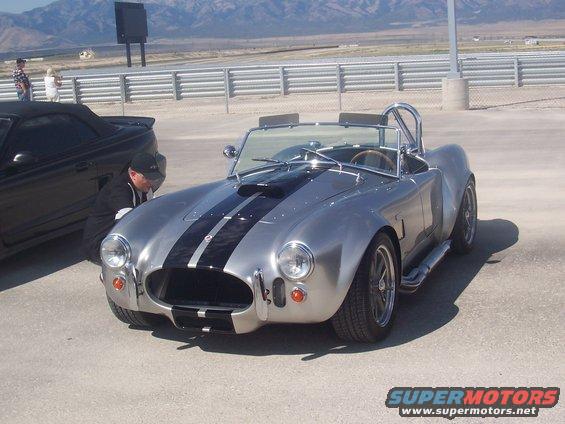 Silver Shelby Cobra replica with black stripes parked next to a black convertible