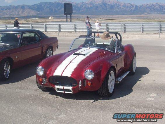 Red convertible sports car with white stripes parked next to a dark coupe. Mountains in background