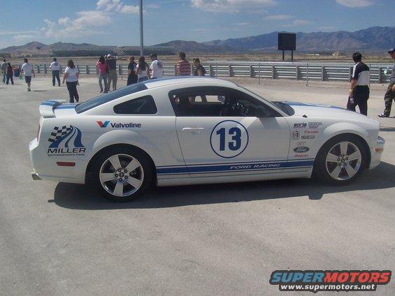 White Ford Mustang with blue racing stripes and number 13 on door, seen from the front three-quarter view