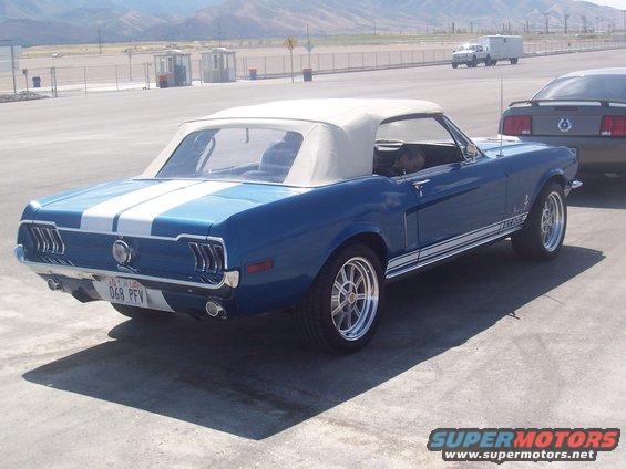Blue convertible classic car with white racing stripes and a tan top parked next to another car