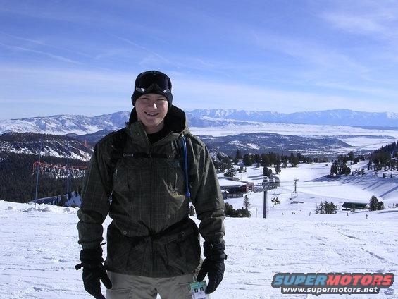 Skier in a green jacket on a snowy mountain with ski lifts and distant mountains