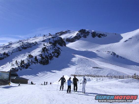 Ski resort with skiers on a sunny day, mountains in background
