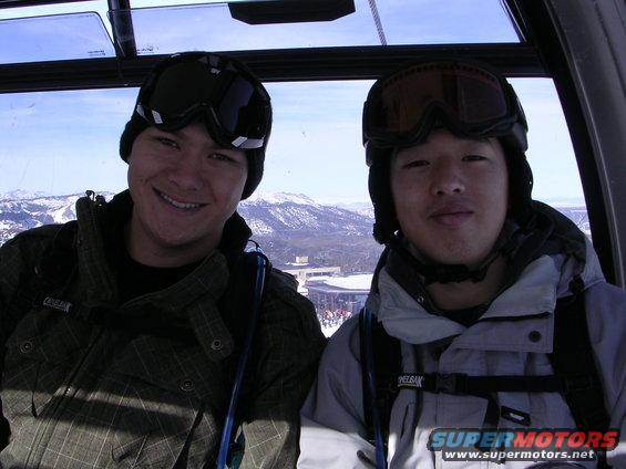 Two men in ski gear smile inside a ski lift with snowy mountains in the background