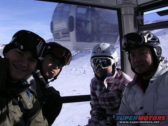 Four people in ski gear inside a gondola with a snowy mountain view