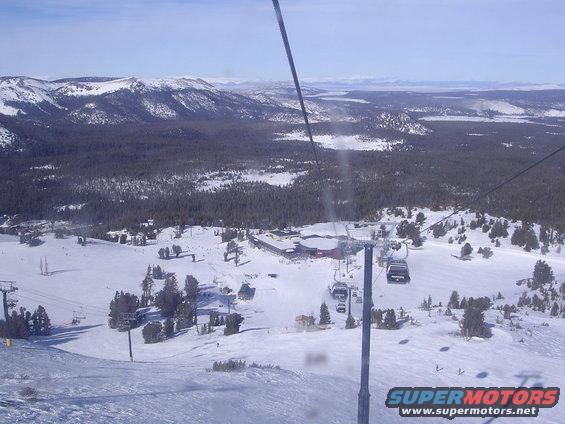 View from a ski lift overlooking a snowy mountain landscape with ski slopes and buildings below