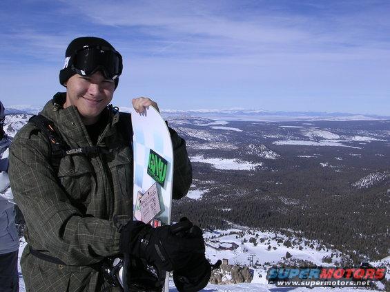 Guy holding snowboard on mountain with snowy landscape and blue sky