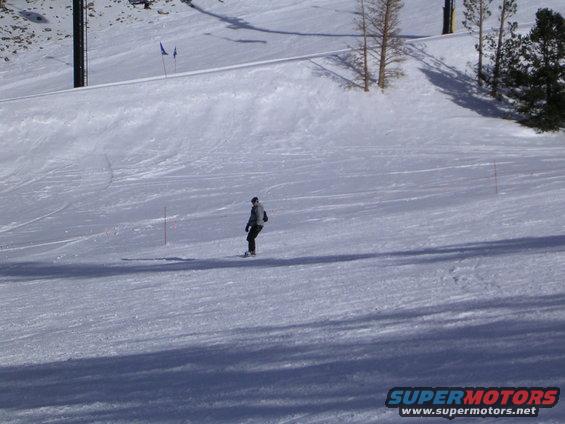 Skier on a groomed ski slope with trees and ski lift in background