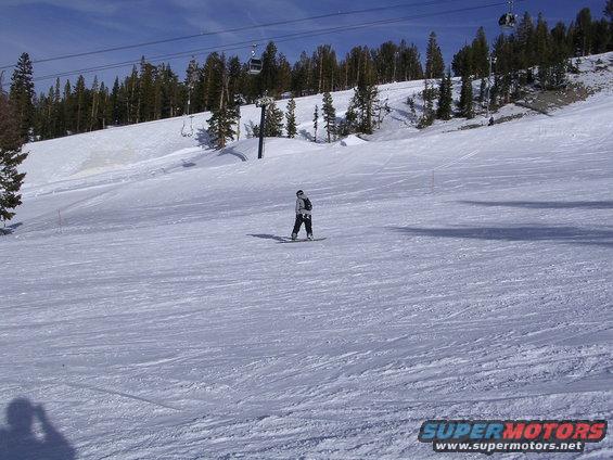 Snowy ski slope with a lone snowboarder and ski lift towers under a blue sky
