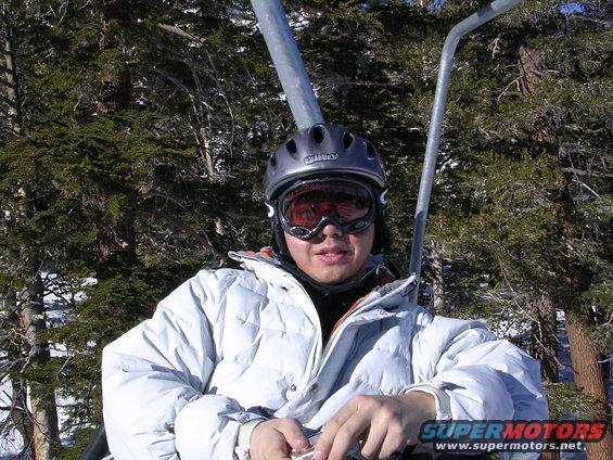 Person in ski gear on a chairlift with trees and snow in background