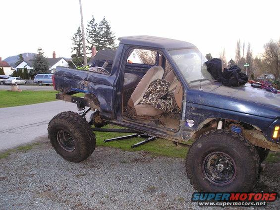 Blue pickup truck with lifted suspension, off-road tires, and missing body panels