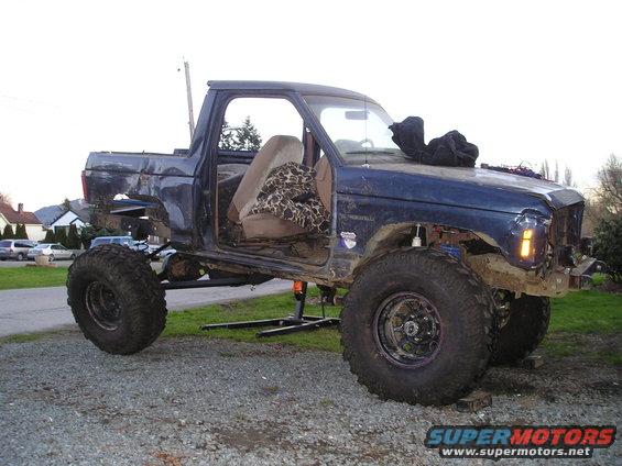 Blue pickup truck with removed doors and body panels, lifted suspension, and large off-road tires