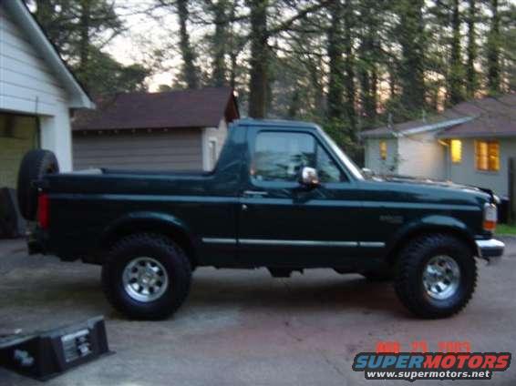 Dark green Ford Bronco with a spare tire on the back, seen from the side