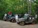 1995 Ford Bronco - Several off-road vehicles are parked on a dirt path in a wooded area, with people standing around and on them.