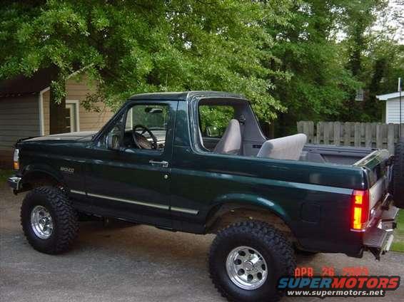 Dark green 1995 Ford Bronco with lifted suspension and aftermarket wheels parked outside