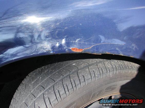 Close-up of a blue car's fender showing scratches and rust near the wheel well