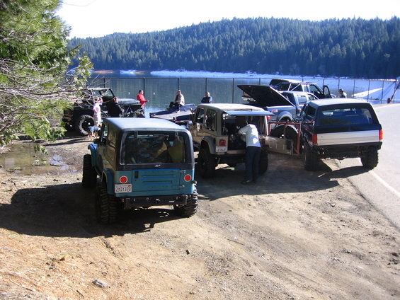 Several Jeeps and a truck parked near a lake with people around