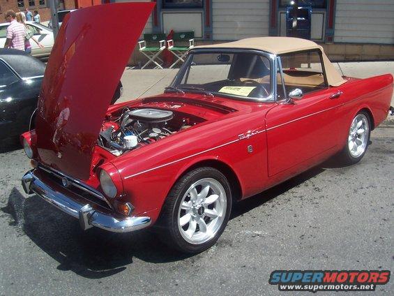 red convertible sports car with hood open showing engine, tan top, aftermarket wheels