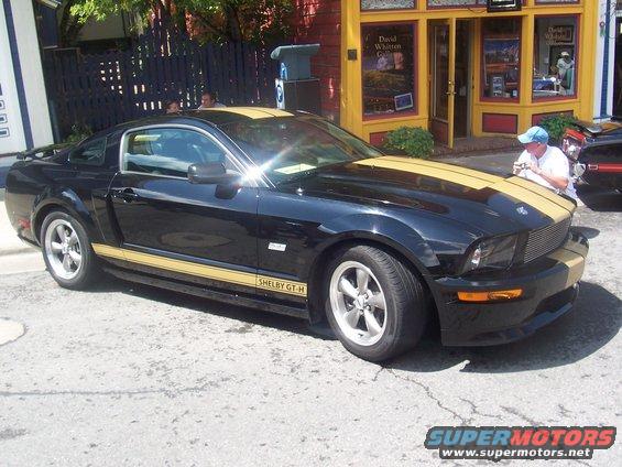 Black Shelby GT-H Mustang with gold stripes parked on street