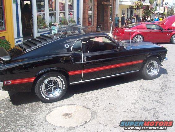 Black 1969 Ford Mustang with red stripe, parked next to a red Ford Mustang