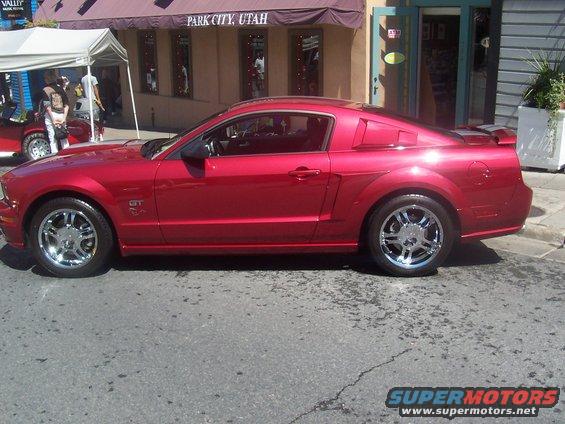 Red Ford Mustang parked on street, side view. GT badge visible