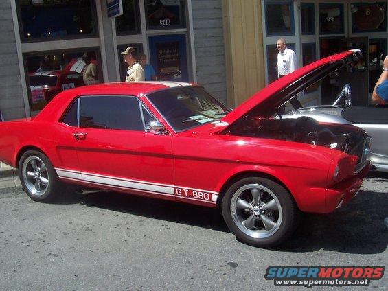 Red 1965 Mustang coupe with white stripes and "G.T. 680" decal, hood open