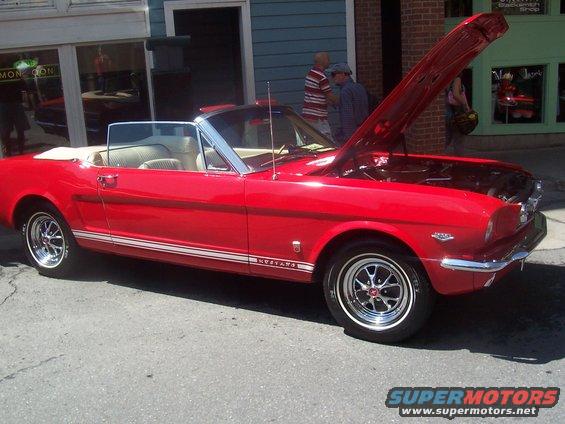 Red convertible classic car with white stripe on side, hood open. Appears to be a 1965 Ford Mustang