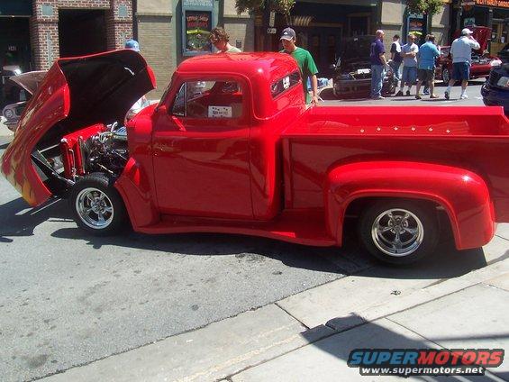 Red pickup truck with hood open, showing engine. Other vehicles and people in background