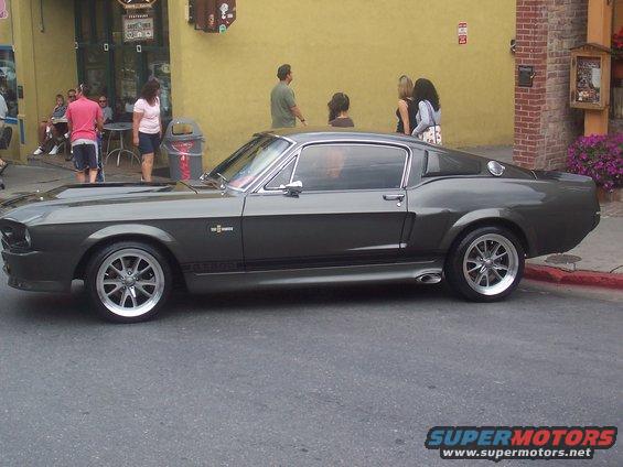 Dark gray coupe with racing stripes and chrome wheels parked on a street