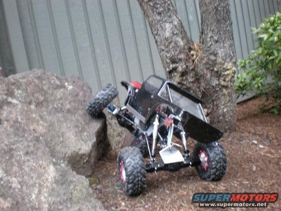 black remote control rock crawler climbing over a rock near a tree