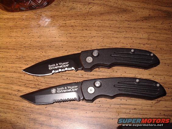 Two black Smith & Wesson Extreme Ops folding knives on a wooden surface