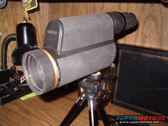 Spotting scope on a small tripod, with a black lamp and a book in the background