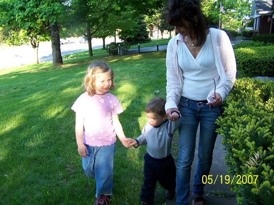 Woman holding hands with two children walking on a grassy path next to bushes, timestamp 05/19/2007