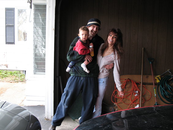 Man holding a baby, with a woman standing next to him in a garage
