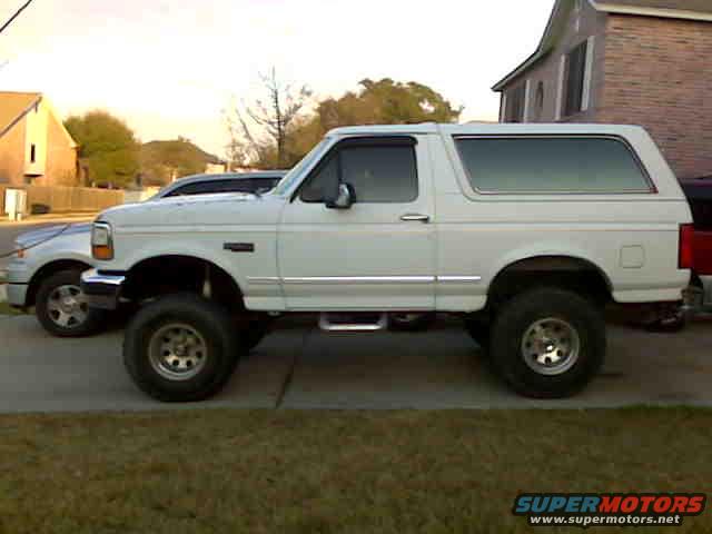 White Ford Bronco with lifted suspension and aftermarket wheels parked next to a silver sedan