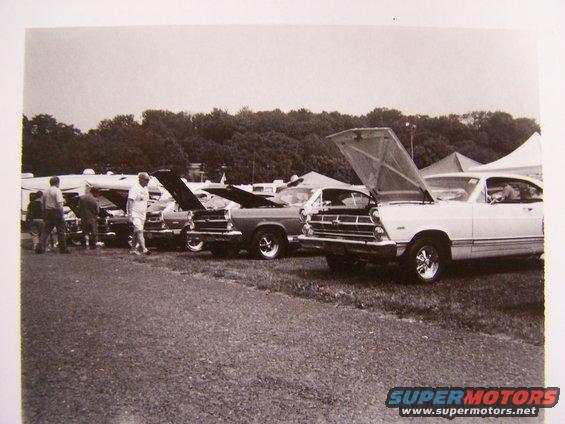 White Ford Ranchero with hood open, parked in a line of cars