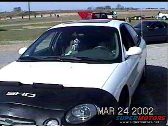 White sedan with black car cover showing 'SHO' logo, seen on March 24, 2002