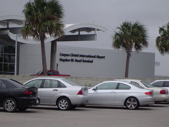 Corpus Christi International Airport terminal with parked cars and palm trees
