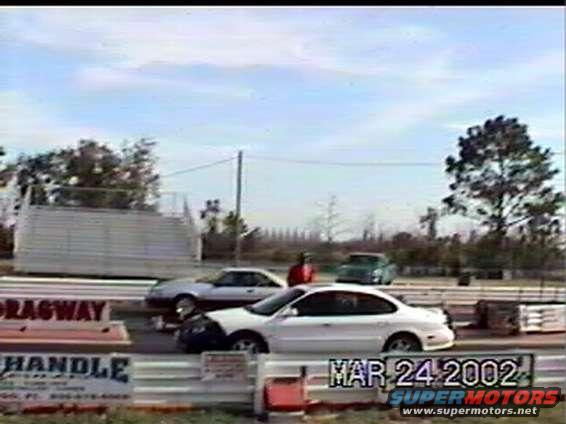 White sedan with a black hood on a drag strip, side view