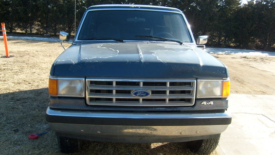Dark blue Ford truck front view. Paint is peeling on the hood. Grille has horizontal bars and a Ford logo. '4x4' badge is visible