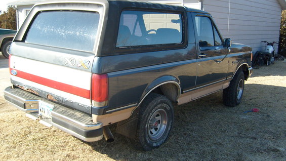 Dark gray Ford Bronco with tan lower body trim, rear quarter view. Red stripe on tailgate