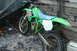 1990 Kawasaki KX125-K2 - A green dirt bike with a blue seat is parked next to a wooden wall, partially covered by a tarp.