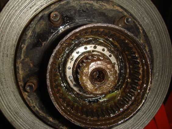 Close-up of a greasy wheel hub assembly and brake rotor, showing internal gears and splines